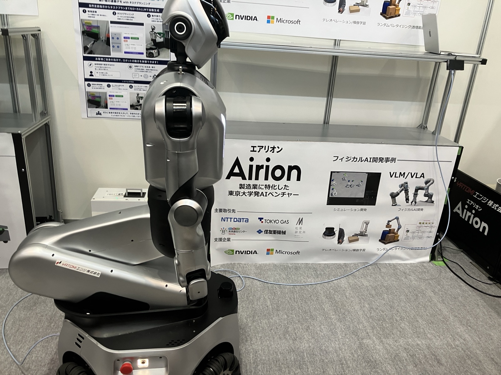 2026年ものづくりワールド東京のAirion展示ブース。移動台車に搭載されたロボットと、VLM・VLAやシミュレーション開発を紹介するパネル